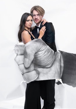 Claudia Sulewski and Finneas posing in front of an image of a hand in a photo by JR