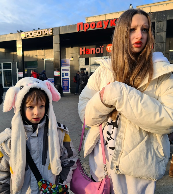 A teenage girl and a little boy with luggage at a train station in Ukraine