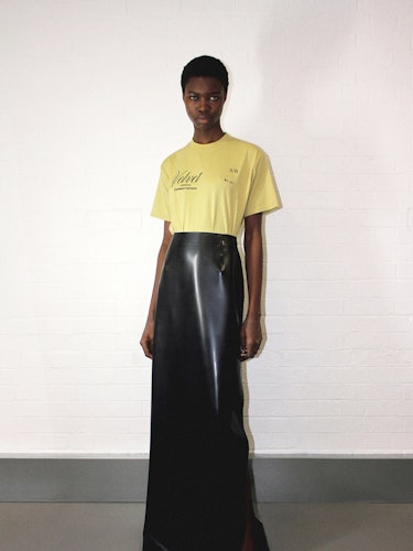 a model wearing a yellow Kwaidan Editions t shirt and black long maxi skirt