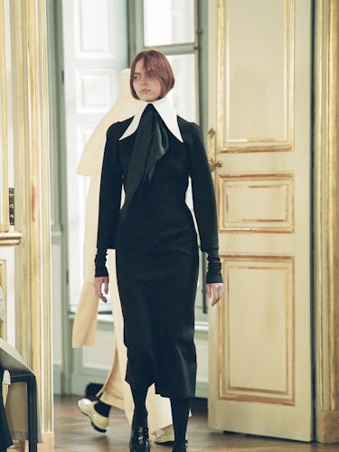 a model walking The Row runway show in a black dress with white high collar