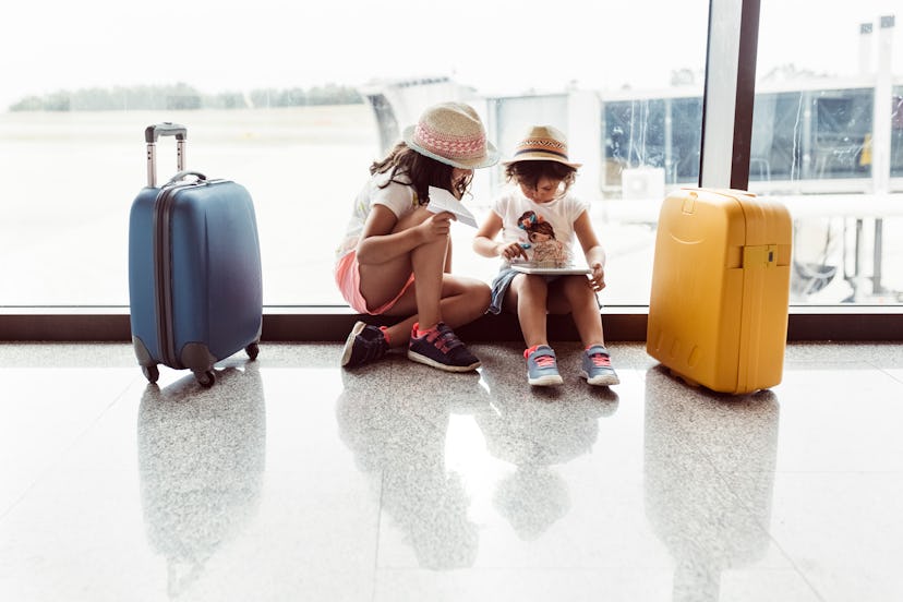 two children waiting at the airport with suitcases