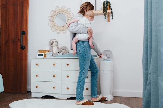 A woman holding her baby and throwing a diaper into her diaper pail at the same time 
