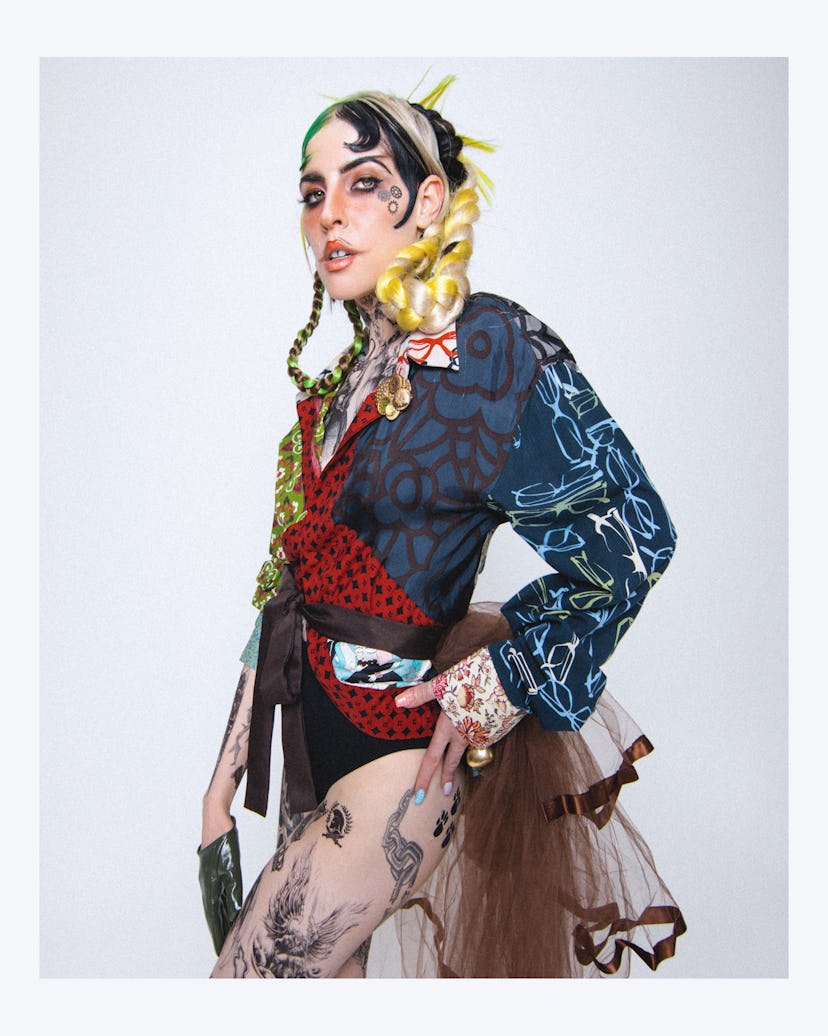 Dorian Electra posing with green-yellow elements in braid, a multi-colored top, leggings with print ...