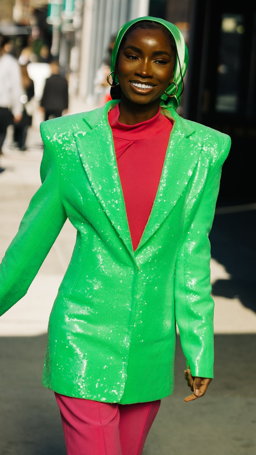 A girl wears a pink turtleneck, matching pants, a green sequin blazer, and a silk headscarf.