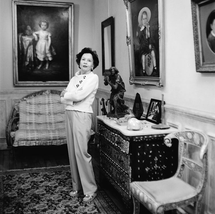 actress Leslie Caron in a white sweater and khakis posing in her living room