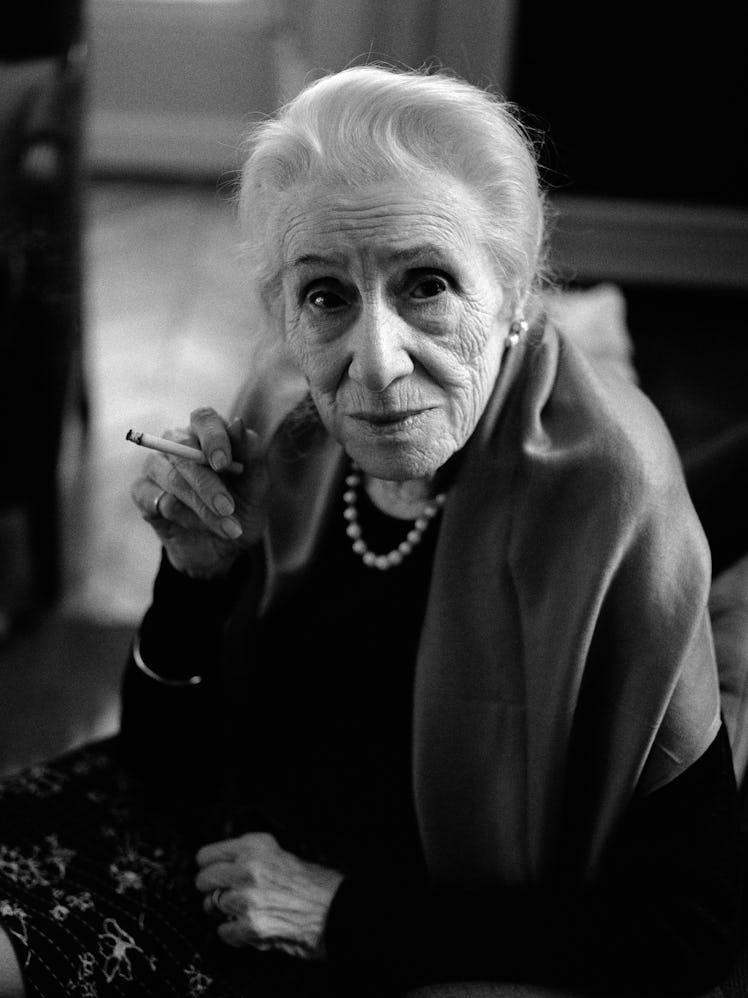 A woman with white hair holding a cigarette and wearing a pearl necklace
