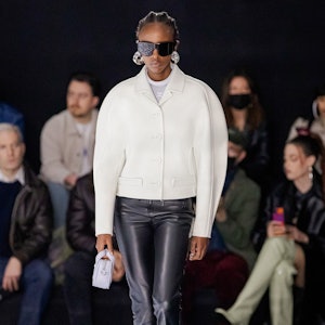 A model wearing a curved white jacket and black leather pants on the Courrèges runway