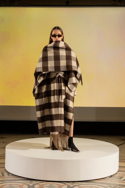 a model wearing a checked cape coat with fringe by Nanushka