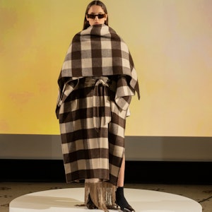 a model wearing a checked cape coat with fringe by Nanushka