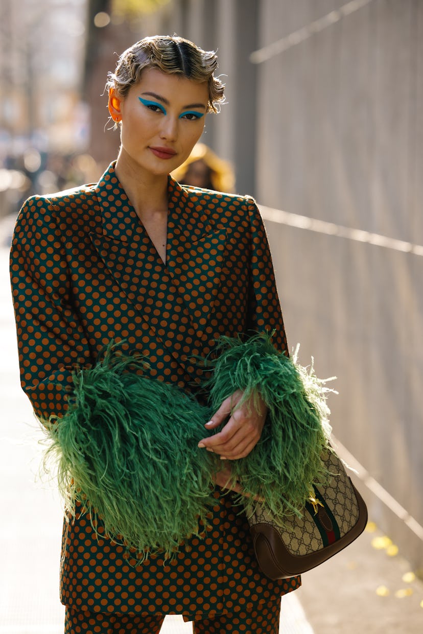 Street style from Milan Fashion Week fall 2022 with green feather jacket and blue eyeshadow. 