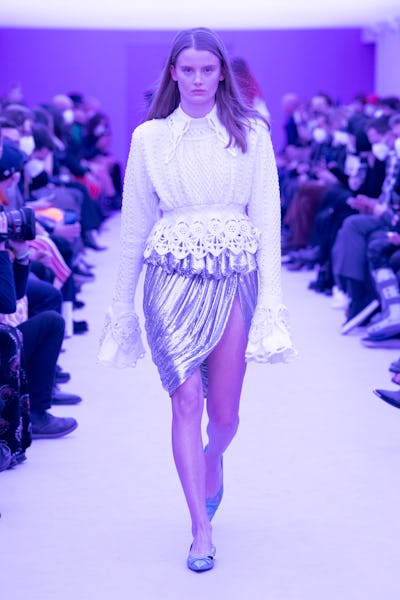 a model wearing a white peplum blouse and silver skirt on the Paco Rabanne runway