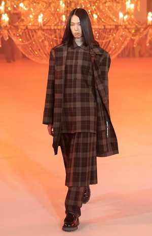 a model wearing a checked jacket, top, and skirt over pants on the Off-White runway