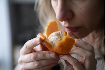 A woman with COVID-19 symptoms tries to sense the smell of a fresh tangerine.