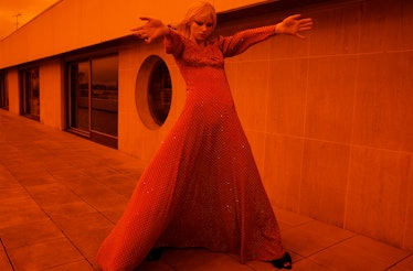 An orange-tinted photo of a person in a dress with outstretched hands