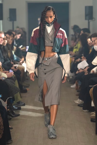 a model wearing a cropped blazer and pencil skirt with a varsity windbreaker jacket on the Rokh runw...