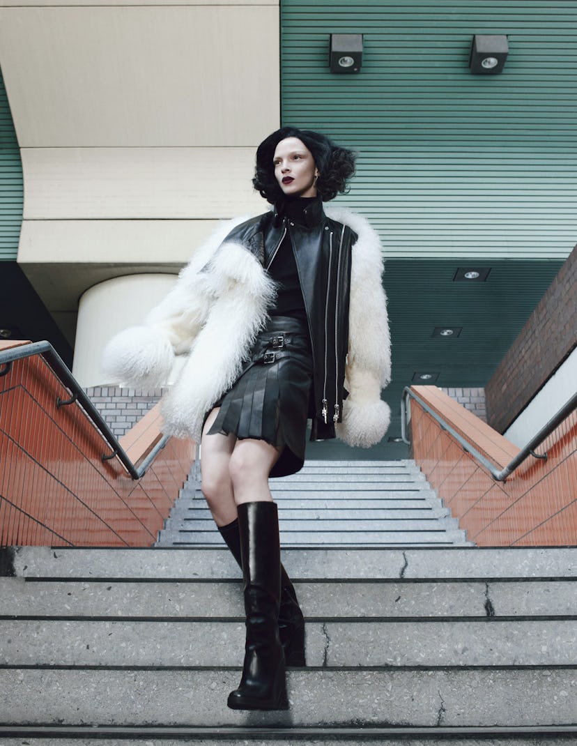 A model in a black leather jacket and matching skirt with a white fur coat over it all 