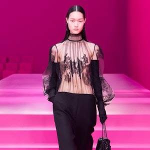 a model wearing a sheer black lace blouse and black trousers on the Valentino runway