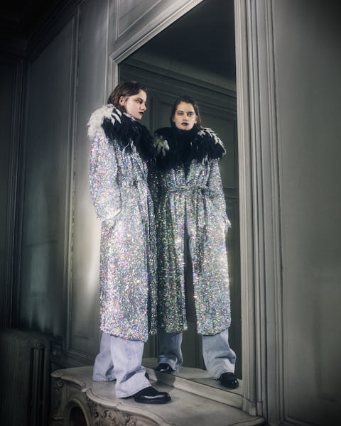 a model wearing a silver sequin coat with a black feather collar by Dries Van Noten