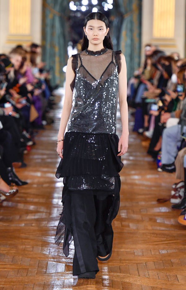 a model sheer black and silver sequin dress over black trousers on the Sacai runway