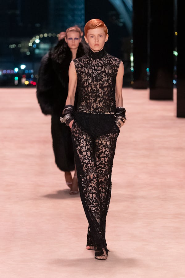 a model wearing a sheer black lace dress on the Saint Laurent runway