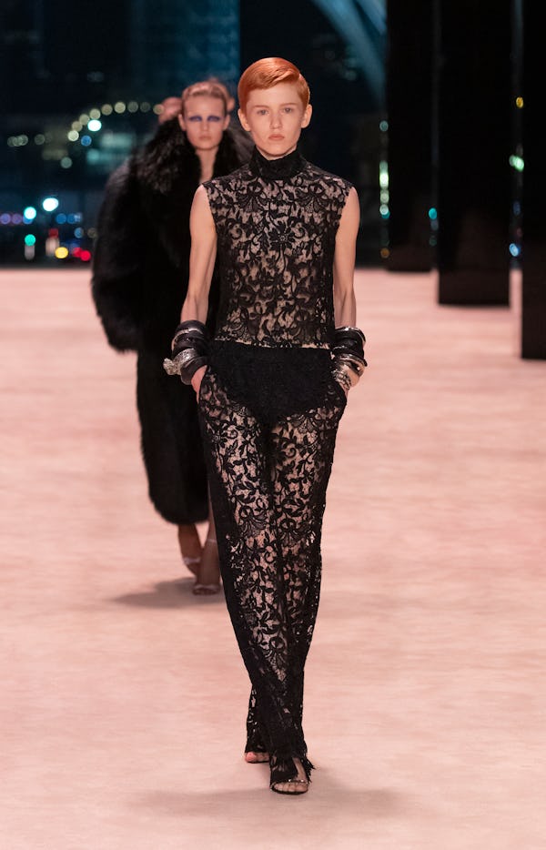 a model wearing a sheer black lace dress on the Saint Laurent runway