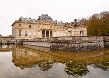 the exterior of a large french chateau, which sits over a shallow body of water