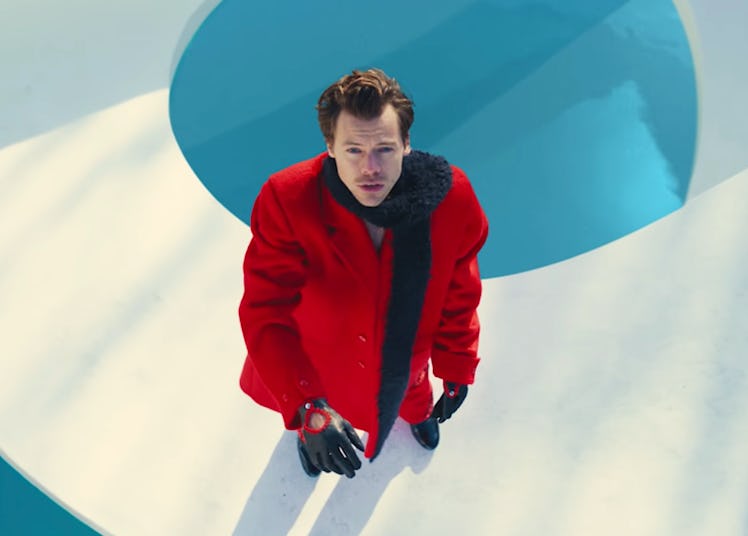 Harry Styles, wearing a red coat and black scarf and gloves, looking up in his 'As It Was' music vid...