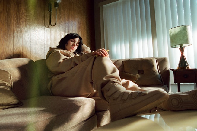 Billie Eilish in a living room wearing her very own designed outfit; beige sweatpants and hoodie and...