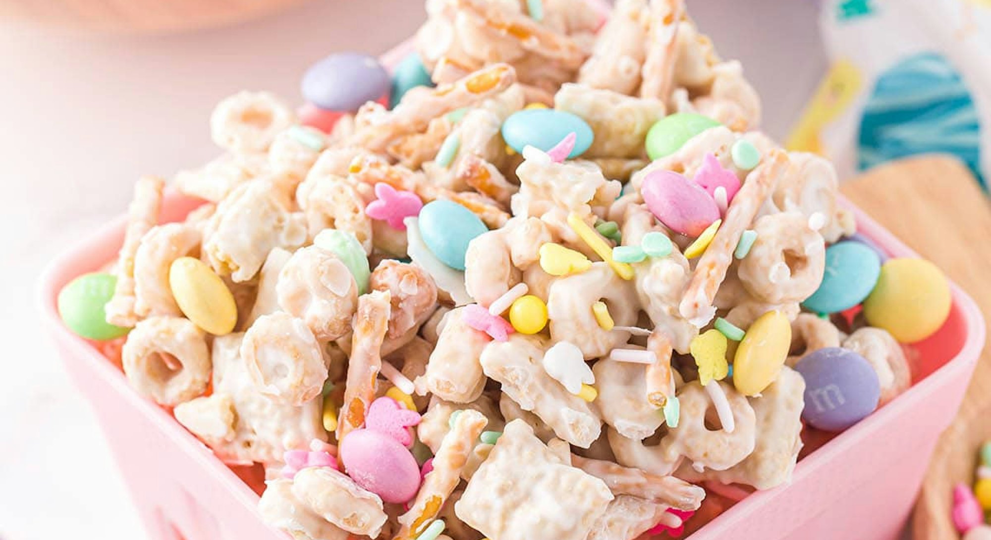 Pink basket with a mix of Chex Mix, Cheerios, pretzels, M&Ms, butterscotch chips, and white chocolat...