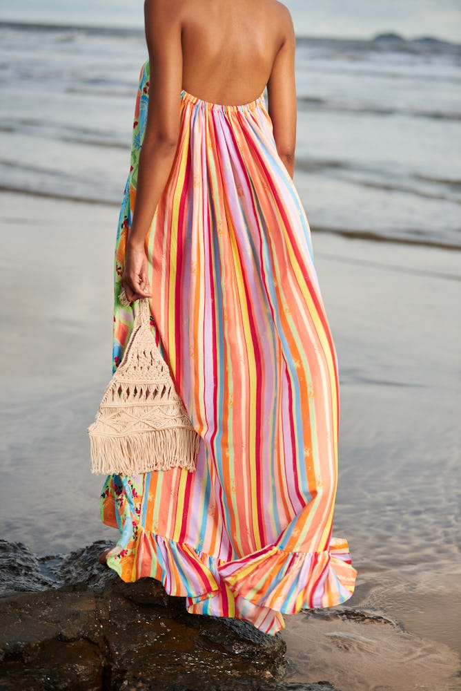 a model wearing a multicolor striped maxi dress with a crochet bag on the beach