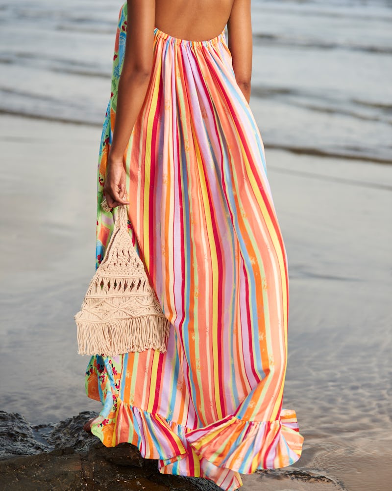 a model wearing a multicolor striped maxi dress with a crochet bag on the beach
