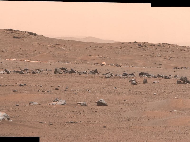 The parachute of the Perseverance rover lies on the Martian regolith in the distance.