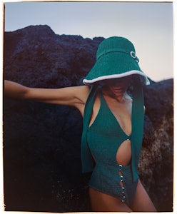 a model wearing a green cutout bathing suit and bucket hat