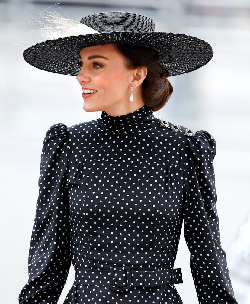 Kate Middleton wears a large black brimmed hat with feathered detail and low chignon while attending...