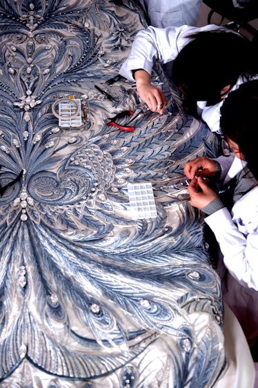 TWo couturiers embroidering a piece of clothing by hand.
