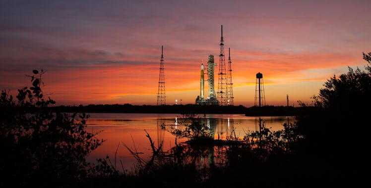 A tall rocket is seen against a red and purple sunset.
