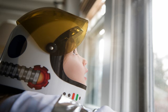A girl dressed as an astronaut looking through a window