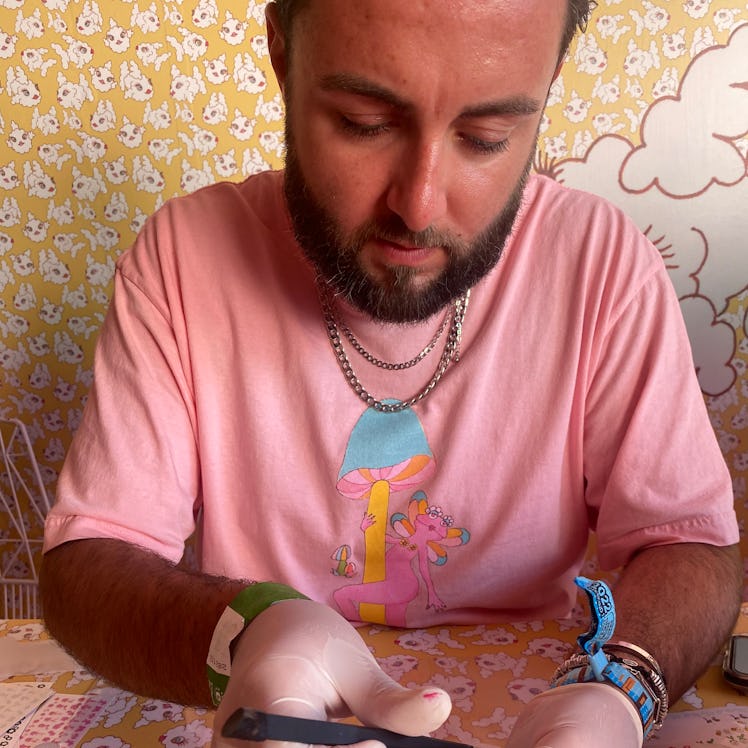 A manicurist wearing a pink Pleasing t-shirt adds a flower decal to a client's pink nail. 