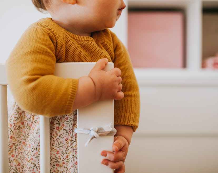 Midriff of a baby holding a bumper protected crib who may not have taken a nap at day care.