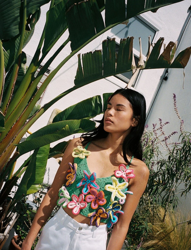 A model standing next to a coconut tree in white bottoms and a top with big flowers on it