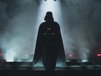 Darth Vader walking through a dark room with smoke in the background in the Obi-Wan Kenobi series
