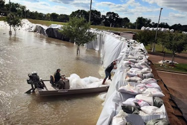 two men in a boat prop up a flooding dam with sandbags
