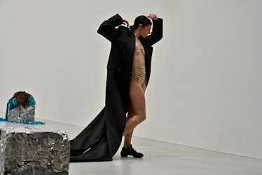A dancer wearing nude undergarments and an oversized black coat. 