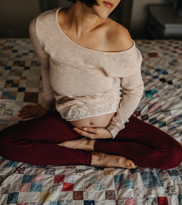 pregnant woman sitting on bed, cradling her belly, should she celebrate mother's day if she's pregna...
