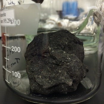 chunk of meteorite in a glass cylinder on top of a table in a lab
