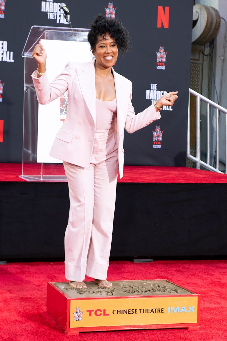 regina king wearing blush pink suit while printing her hands and feet at tcl chinese theatre in holl...