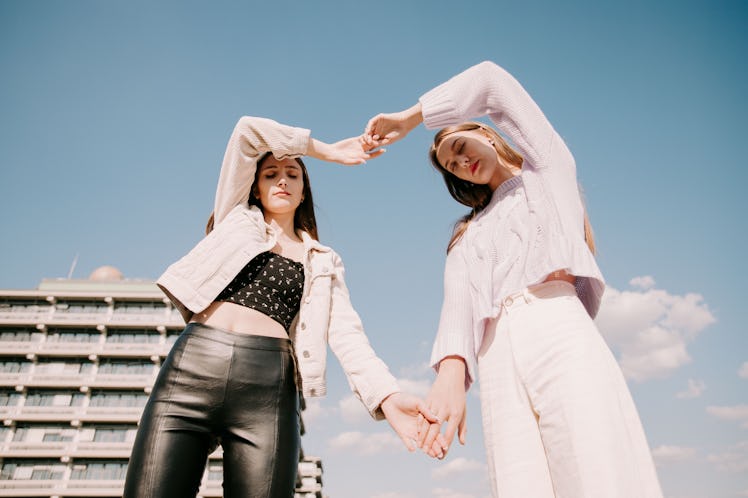 Two young women making a heart shape out of their arms before reading their May 2022 horoscope.