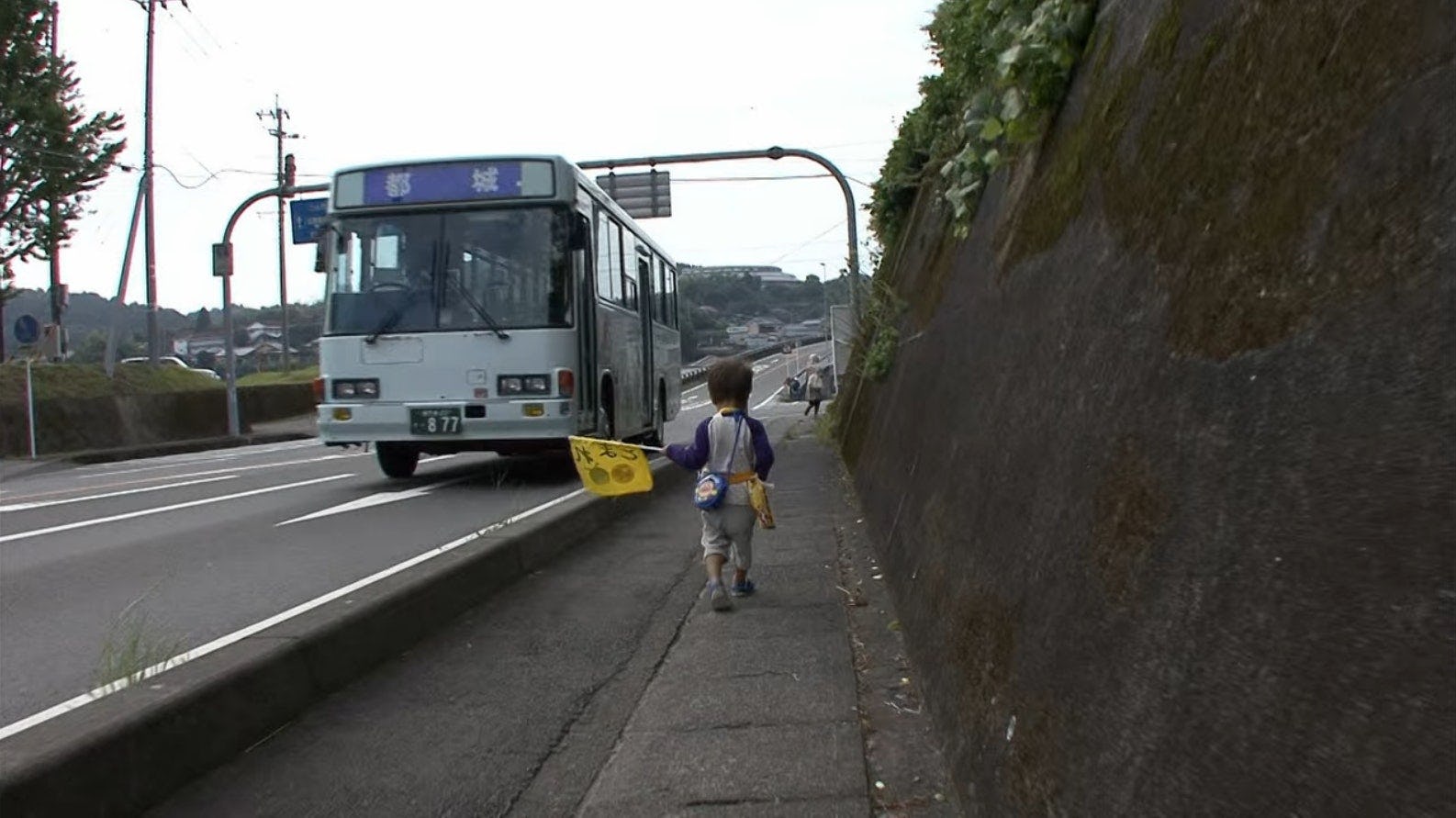 A toddler on 'Old Enough' walks down a small town street.