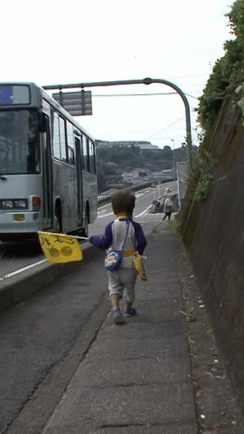 A toddler on 'Old Enough' walks down a small town street.