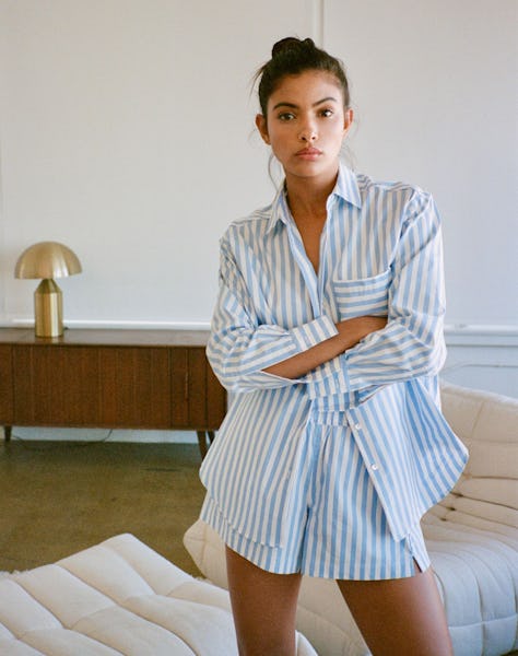 a model wearing an oversize striped button-down shirt with jeans and flats on the beach